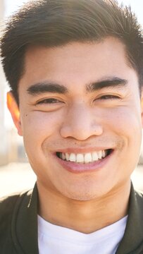 Outdoor Vertical portrait of a smiling Chinese guy looking at the camera laughing with positive face and friendly look. Close up of a Happy human face - Cheerful Asian young man. People and emotions.