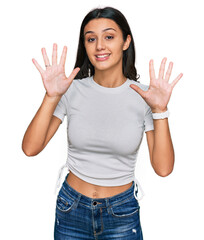 Young hispanic girl wearing casual white t shirt showing and pointing up with fingers number ten while smiling confident and happy.