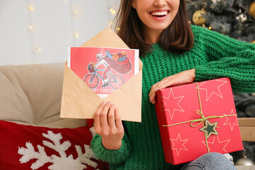Woman with gift box and Christmas greeting card in envelope at home, closeup