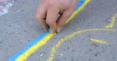 Drawings on the asphalt to decorate public spaces and add color to the urban environment, means of conveying a message or idea. Street artists hand close up, creating yellow and blue stripes.