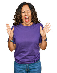 Middle age hispanic woman wearing casual clothes celebrating mad and crazy for success with arms...