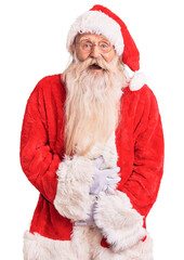 Old senior man with grey hair and long beard wearing traditional santa claus costume smiling and laughing hard out loud because funny crazy joke with hands on body.