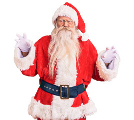 Old senior man with grey hair and long beard wearing traditional santa claus costume smiling funny doing claw gesture as cat, aggressive and sexy expression