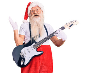 Old senior man with grey hair and long beard wearing santa claus costume playing electric guitar celebrating victory with happy smile and winner expression with raised hands
