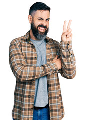 Hispanic man with beard wearing casual shirt smiling with happy face winking at the camera doing...