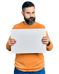 Hispanic man with beard holding blank empty banner skeptic and nervous, frowning upset because of problem. negative person.
