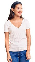 Obraz premium Young beautiful latin girl wearing casual white t shirt looking away to side with smile on face, natural expression. laughing confident.