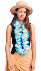 Young beautiful latin girl wearing hawaiian lei and summer hat skeptic and nervous, frowning upset...