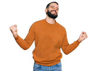 Young man with beard wearing casual winter sweater very happy and excited doing winner gesture with arms raised, smiling and screaming for success. celebration concept.