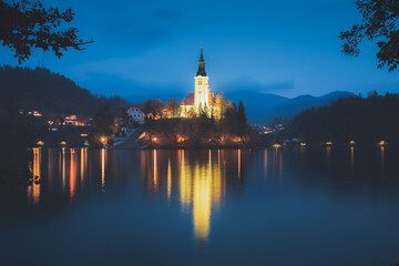 Evening twilight view of Pilgrimage Church of the Assumption of Maria Bled Castle lit up at Lake Bled, Slovenia in the Julian Alps.