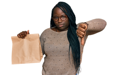 Young black woman with braids holding take away paper bag with angry face, negative sign showing dislike with thumbs down, rejection concept