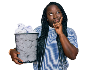 Young black woman with braids holding paper bin full of crumpled papers serious face thinking about question with hand on chin, thoughtful about confusing idea