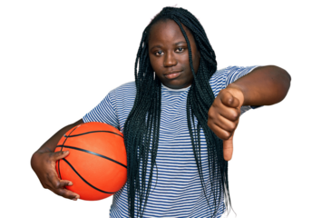 Young black woman with braids holding basketball ball with angry face, negative sign showing dislike with thumbs down, rejection concept