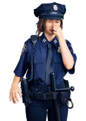 Young beautiful girl wearing police uniform smelling something stinky and disgusting, intolerable smell, holding breath with fingers on nose. bad smell