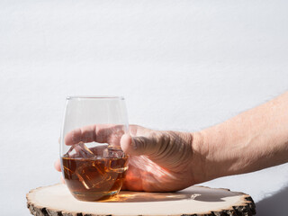 Male hand picking up a glass of iced tea or Alcoholic drink off of a wood table against a white...