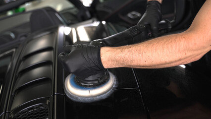 Obraz na płótnie Canvas Schwarzer Supersportwagen wird vom Fahrzeugaufbereiter mit der Poliermaschine poliert 