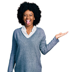 Young african american woman presenting with open palm sticking tongue out happy with funny...