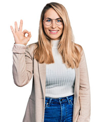 Young blonde woman wearing business shirt and glasses smiling positive doing ok sign with hand and fingers. successful expression.