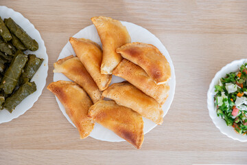 Dish of grape rolls on wooden table from top view with sambousek and qatayef