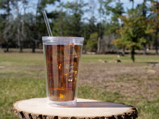 Iced Cold Drink in a plastic cup with a straw on a wood table in a Tourist Resort or Country Club setting.