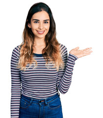 Beautiful hispanic woman wearing casual striped shirt smiling cheerful presenting and pointing with palm of hand looking at the camera.