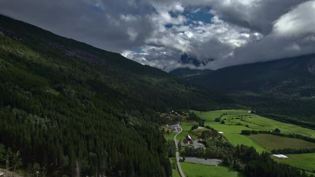 Aerial slider shot over the beautiful green Innerdalen valley in Norway. Meadows and vast forests against the mountains covered with white cumulus clouds. Nordic nature travel concept