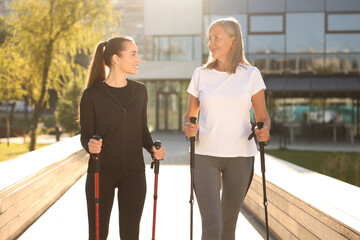 Fototapeta na wymiar Happy women practicing Nordic walking with poles outdoors on sunny day