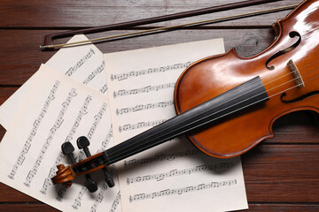 Violin, bow and music sheets on wooden table, top view