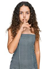 Fototapeta na wymiar Teenager hispanic girl wearing casual clothes asking to be quiet with finger on lips. silence and secret concept.