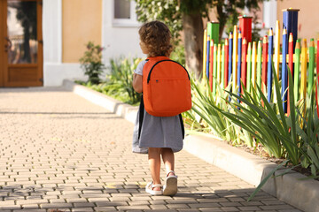 Little girl walking to kindergarten outdoors on sunny day, back view. Space for text - obrazy, fototapety, plakaty