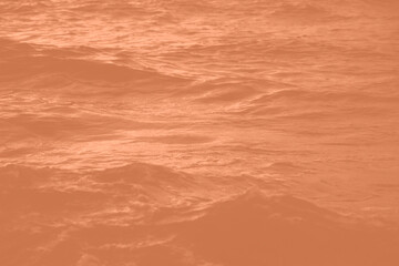 Peach Fuzz toned sea water texture. Pool water with sun reflections. Trendy colour 2024 year.