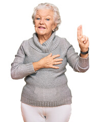 Senior grey-haired woman wearing casual winter sweater smiling swearing with hand on chest and fingers up, making a loyalty promise oath