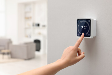 Smart home system. Woman using thermostat indoors, closeup