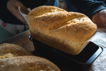 Close up of baker is taking off rye wheat bread from oven, small business bread bakery factory concept