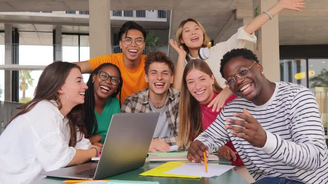 Group of young teenage students waving hands at library, using a laptop, looking at camera. Happy classmates studying and doing homeworks at highschool. Multiracial academy people staring front. High