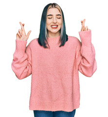 Young modern girl wearing pink wool winter sweater gesturing finger crossed smiling with hope and eyes closed. luck and superstitious concept.