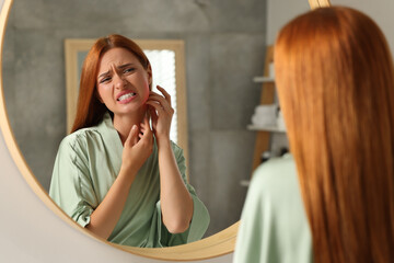 Suffering from allergy. Young woman scratching her neck near mirror in bathroom