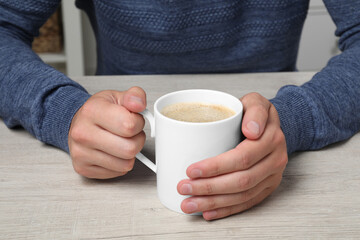 Man with white mug at wooden table, closeup
