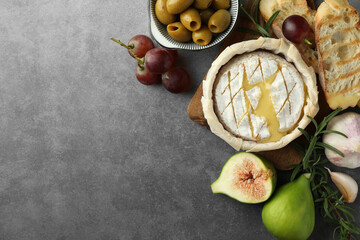 Tasty baked brie cheese and products on grey table, flat lay. Space for text
