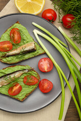 Delicious sandwiches with sprats, tomatoes, avocado puree and dill on wooden table, flat lay
