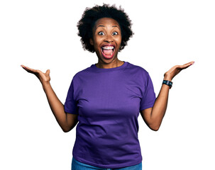 African american woman with afro hair wearing casual purple t shirt celebrating crazy and amazed for success with arms raised and open eyes screaming excited. winner concept