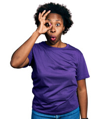 Fototapeta na wymiar African american woman with afro hair wearing casual purple t shirt doing ok gesture shocked with surprised face, eye looking through fingers. unbelieving expression.