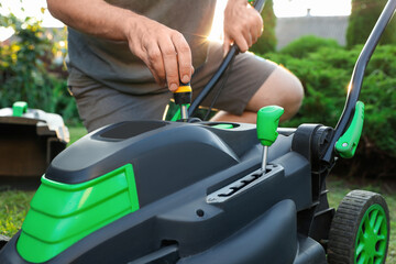 Man with screwdriver fixing lawn mower in garden, closeup - obrazy, fototapety, plakaty