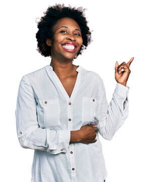 African american woman with afro hair wearing casual white t shirt with a big smile on face, pointing with hand and finger to the side looking at the camera.