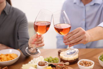 People clinking glasses with rose wine above wooden table indoors, closeup