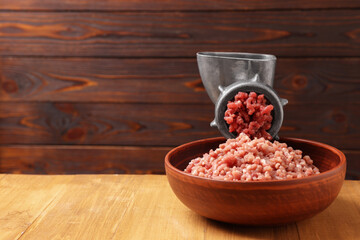 Manual meat grinder with beef mince on wooden table, space for text