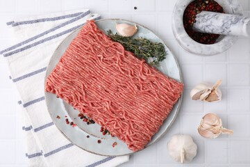 Fresh raw ground meat, peppercorns, garlic and thyme on white tiled table, flat lay