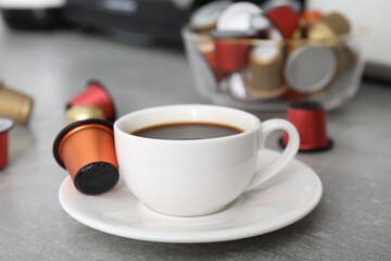 Cup of coffee and capsules on light grey table, closeup