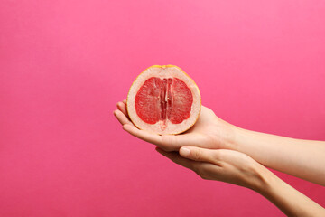Woman holding half of grapefruit on pink background, closeup. Sex concept