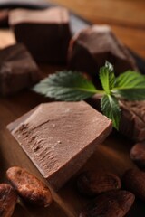 Pieces of tasty milk chocolate, mint and cocoa beans on table, closeup